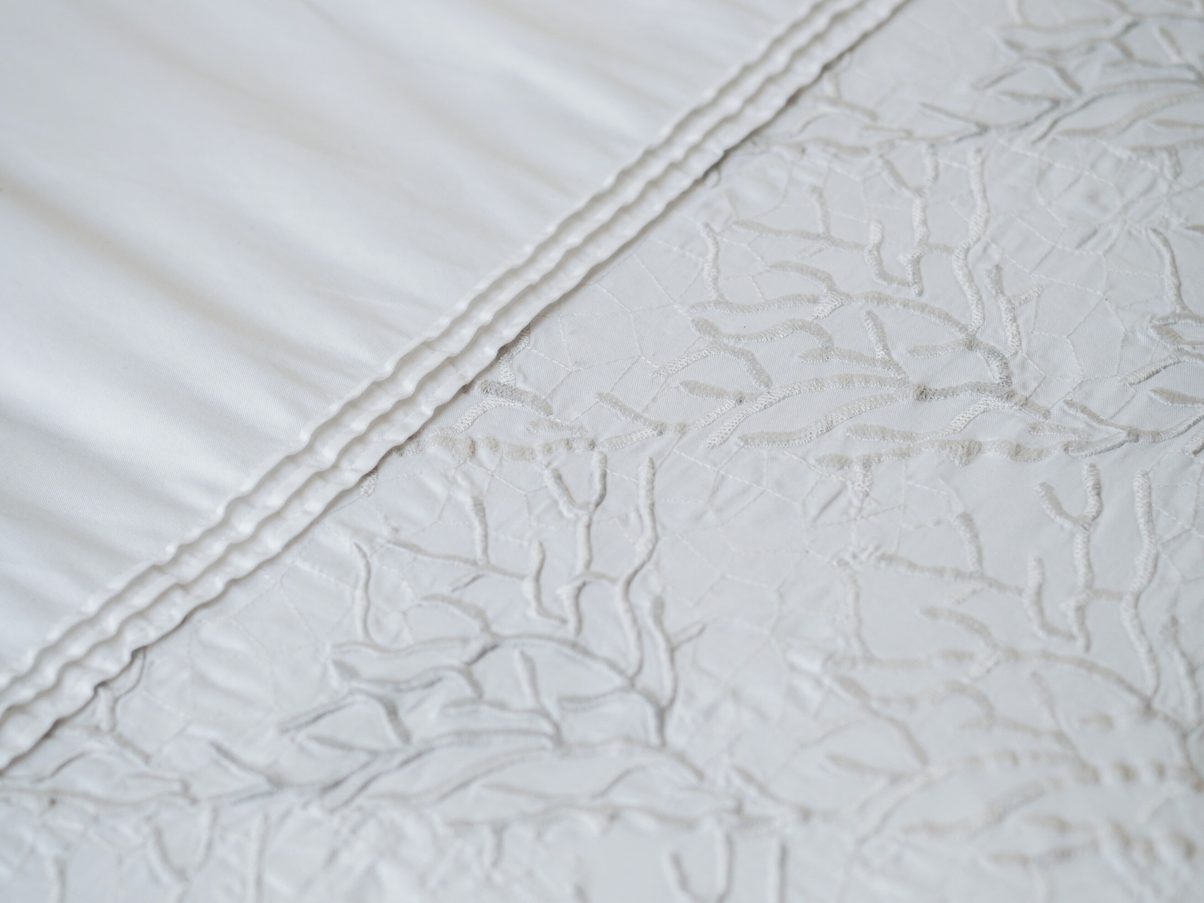 Primer plano de una cama con una colcha blanca y texturizada, y un diseño bordado decorativo.