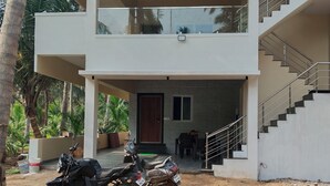 A two-story building with a covered outdoor area, a staircase, and a parked motorcycle. - LIMRA FARM HOUSE  (Anaimalai)