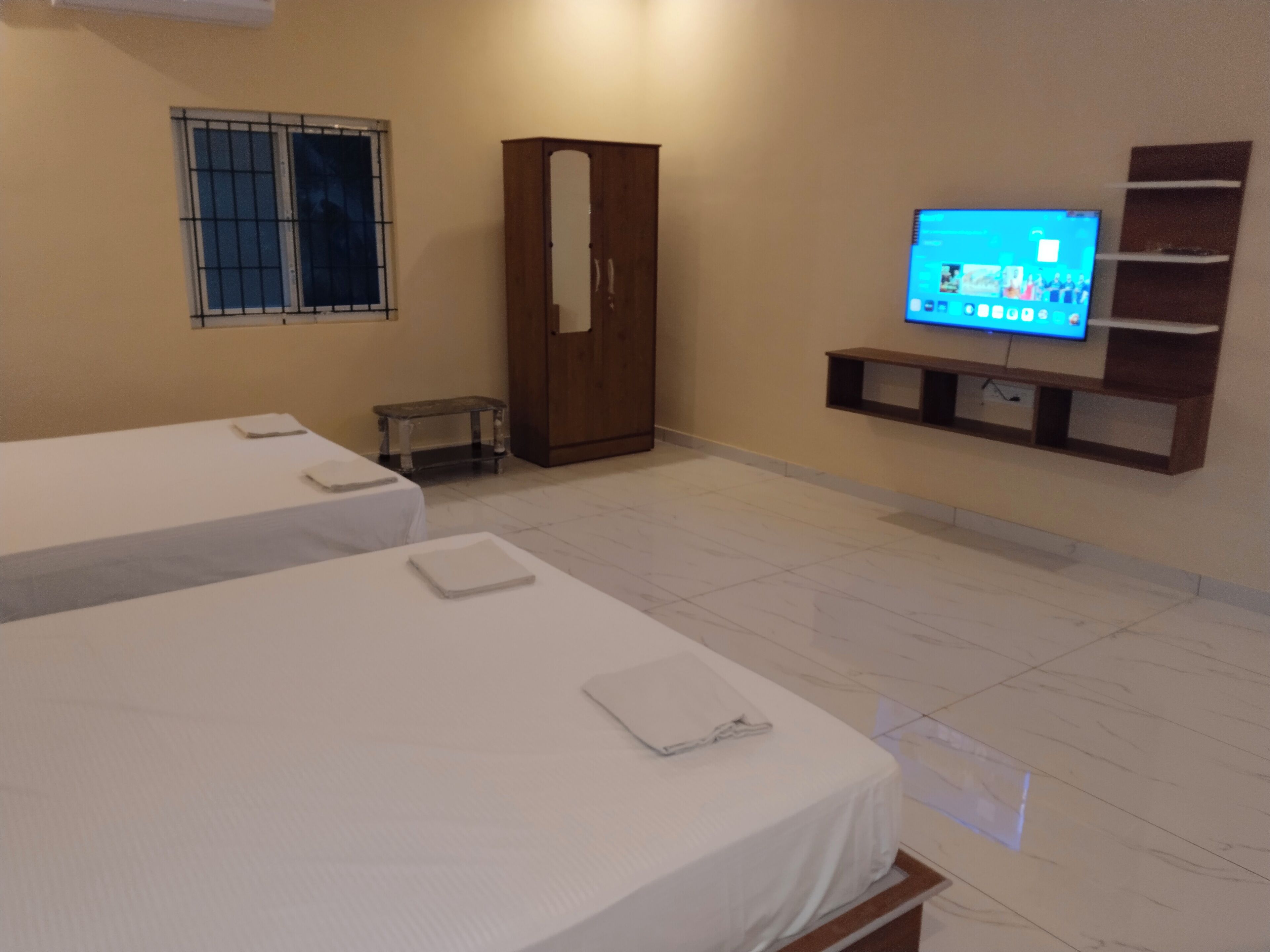 A hotel room with two beds, a wardrobe, a television, and a small table.