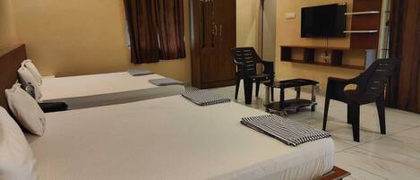 A hotel room with two beds, a TV, a wardrobe, a small table, and two chairs.