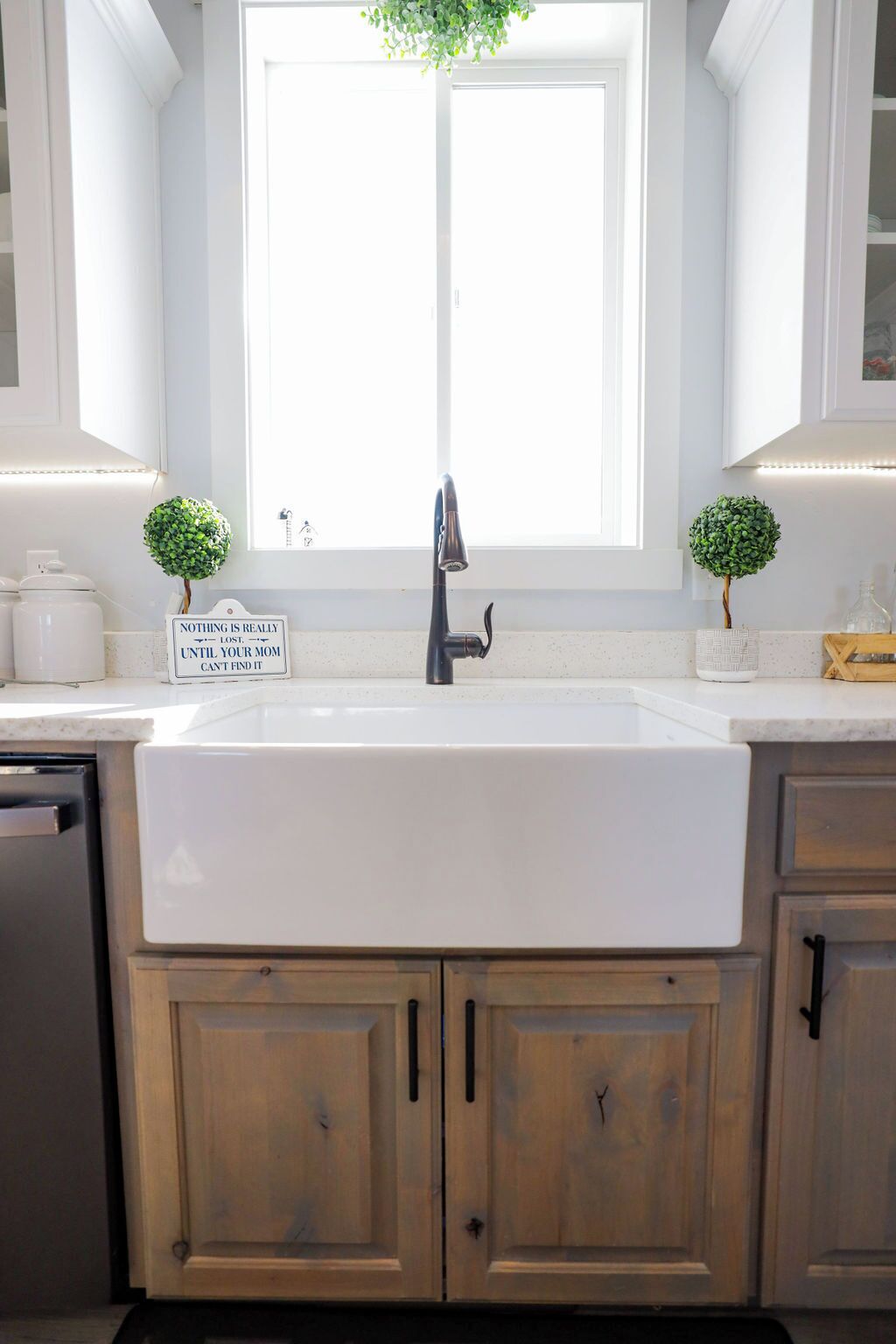Una cocina con un lavabo blanco, armarios de madera y dos pequeñas macetas.