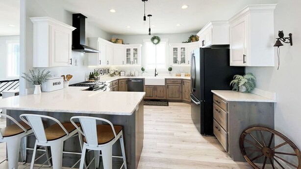 A modern kitchen with white cabinetry, a central island with bar stools, a black refrigerator, and a decorative wagon wheel. - Cozy 6 bedroom home minutes from Rigby Lake (Rigby)