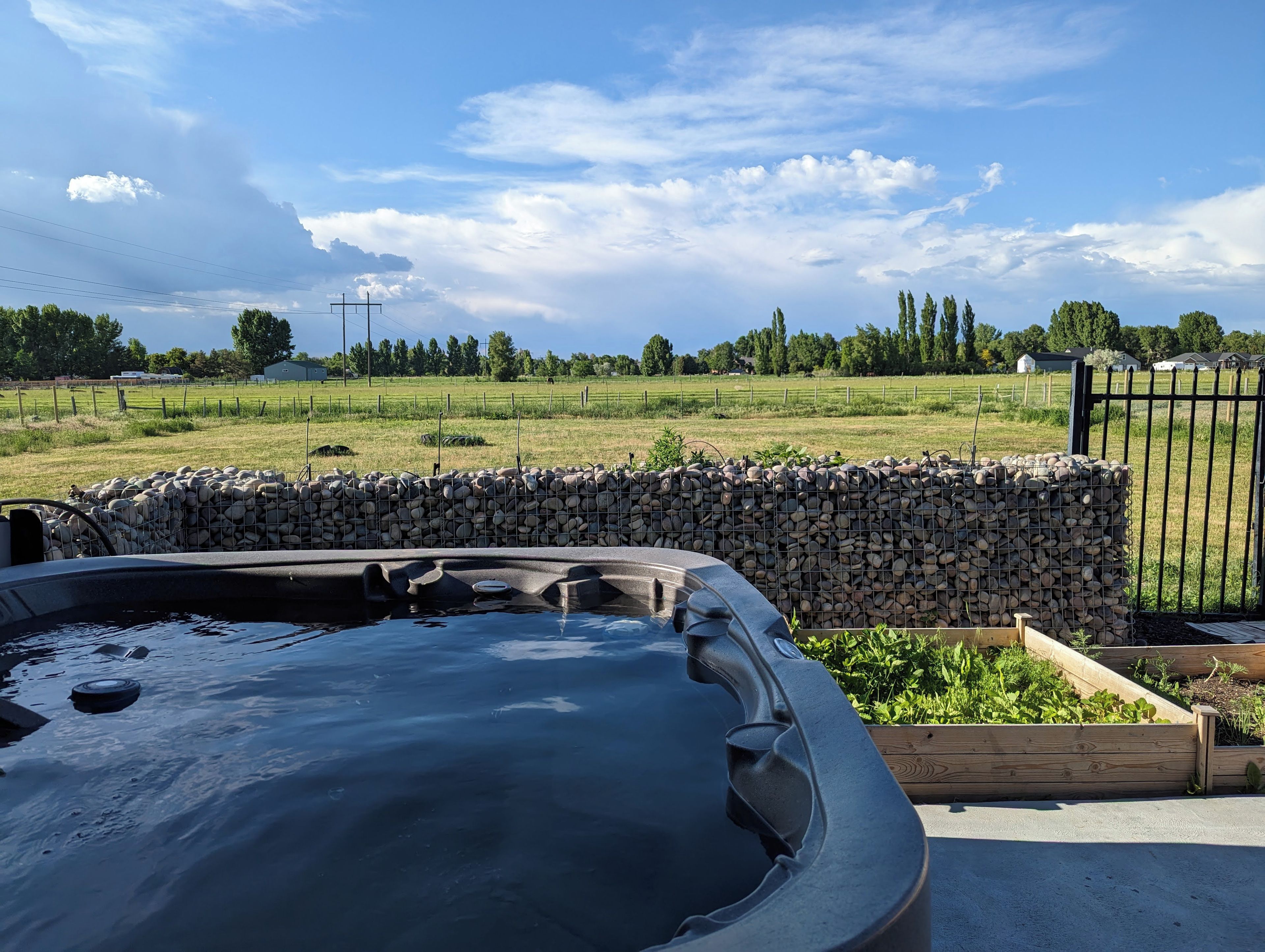 Un jacuzzi installé dans un jardin, avec un mur en pierre et une terrasse en bois.