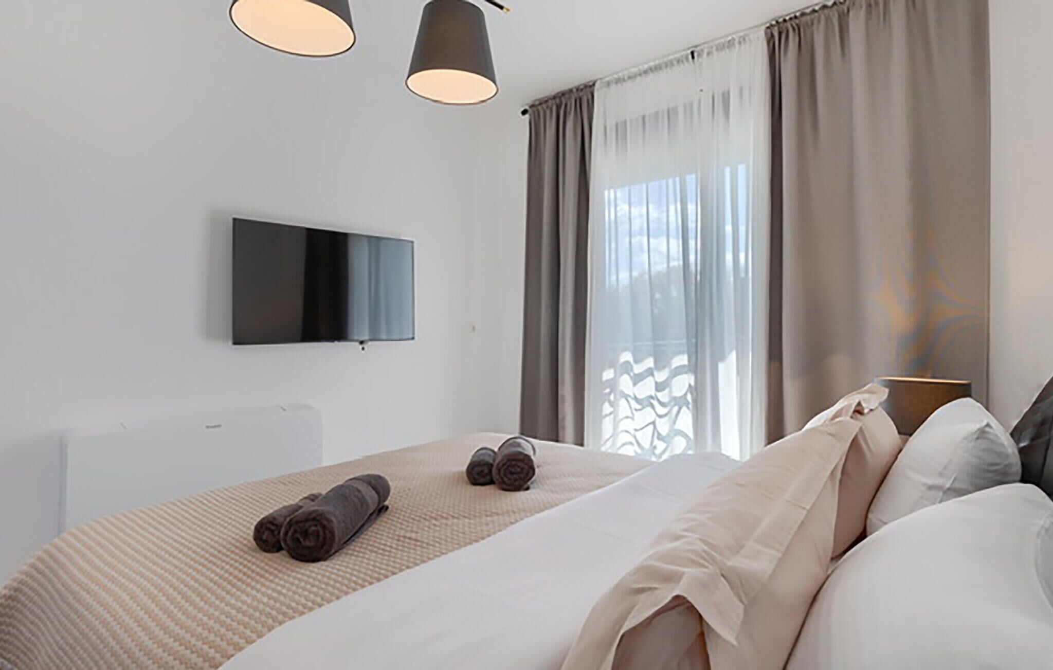 Een moderne hotelkamer met een groot bed, een flatscreen televisie aan de muur en een raam met gordijnen.