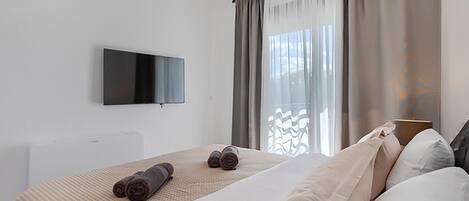 Een moderne hotelkamer met een groot bed, een flatscreen televisie aan de muur en een raam met gordijnen.
