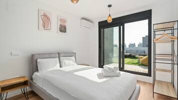 Una habitación de hotel moderna con una cama grande, una mesita de noche de madera, una lámpara colgante y vistas de la ciudad a través de un ventanal.