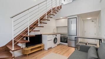 Un apartamento moderno con una escalera de madera, una cocina con lavadora, un comedor y una sala de estar con sofá.