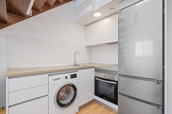 Cocina compacta con lavadora, horno y refrigerador de acero inoxidable.