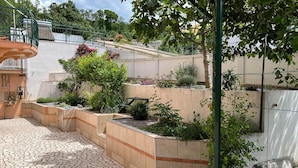 Un patio con suelo de baldosas de piedra, una pequeña fuente y diversas plantas y arbustos.