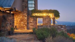 A stone building with a glass window and a wooden pergola covered in foliage.