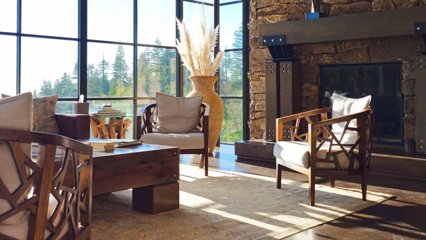 A cozy living room with a fireplace, large windows, and a view of trees.