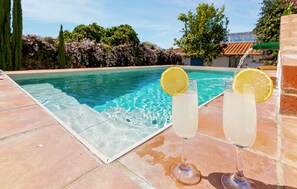 Une piscine, avec deux verres contenant une boisson claire, chacun agrémenté d’une tranche de citron, sur une terrasse carrelée.