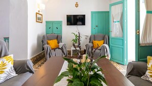 Een kamer met twee fauteuils, een tafel, een flatscreen televisie en deuren in blauwgroen.