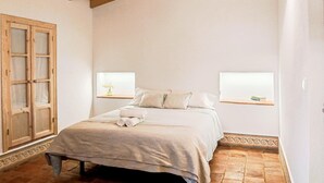 Een slaapkamer met een bed, een houten deur, twee nachtkastjes met lampen en een betegelde vloer.