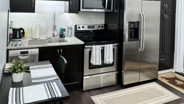 Una cocina moderna con armarios oscuros, electrodomésticos de acero inoxidable y un salpicadero de azulejos.