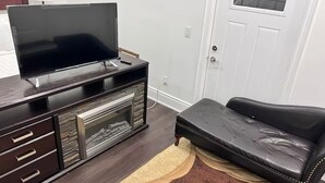 Una sala de estar con un televisor de pantalla plana sobre un mueble bajo de madera oscura, un sofá de cuero negro y un tapete estampado.