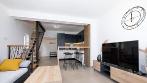 A modern living room with a sofa, a coffee table, a TV, and a staircase leading to a kitchen area.
