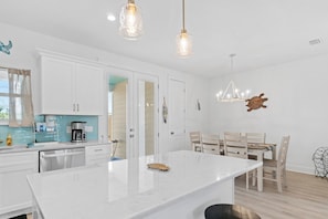 Una cocina moderna con armarios blancos, una isla de mármol e iluminación colgante.