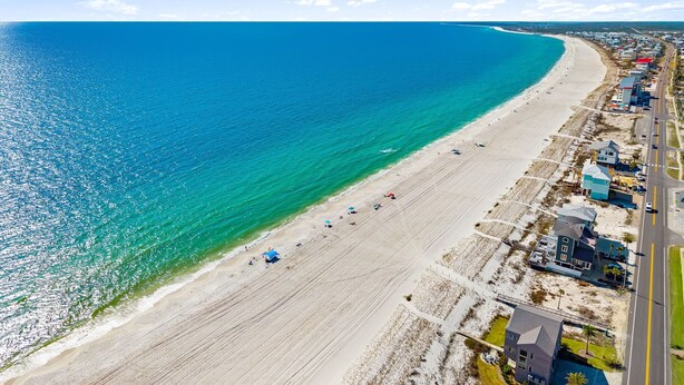 An aerial view of a beach with a road running parallel to the shore, a few buildings, and a clear blue ocean. - 3-Bedroom Gulf Views Retreat - 1 Min to Beach (Mexico Beach)