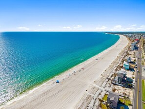 Une vue aérienne d’une plage, avec une route qui longe le rivage, quelques bâtiments et un océan d’un bleu limpide.