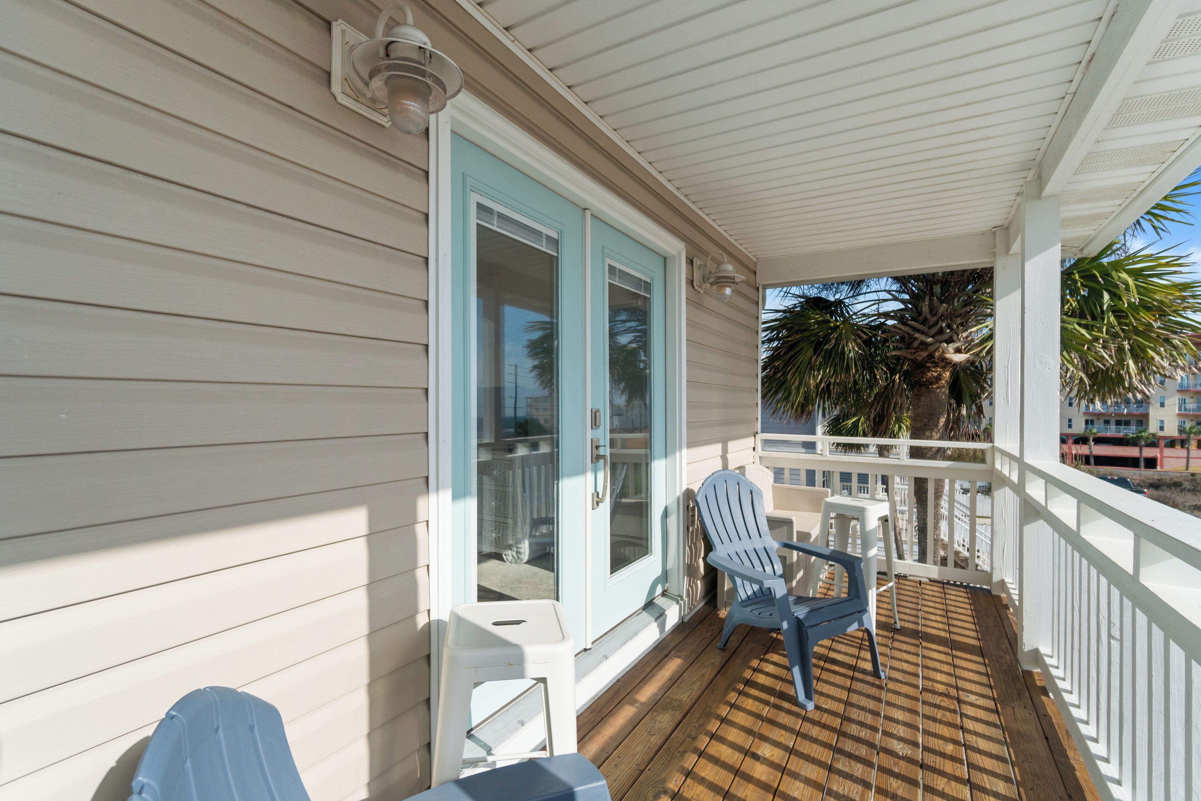 A covered porch with a white railing, two Adirondack chairs, and a small table.
