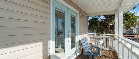 A covered porch with a white railing, two Adirondack chairs, and a small table.