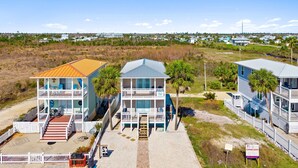 A coastal property with two-story buildings, a covered deck, and a sandy driveway. - 3-Bedroom Gulf Views Retreat - 1 Min to Beach (Mexico Beach)