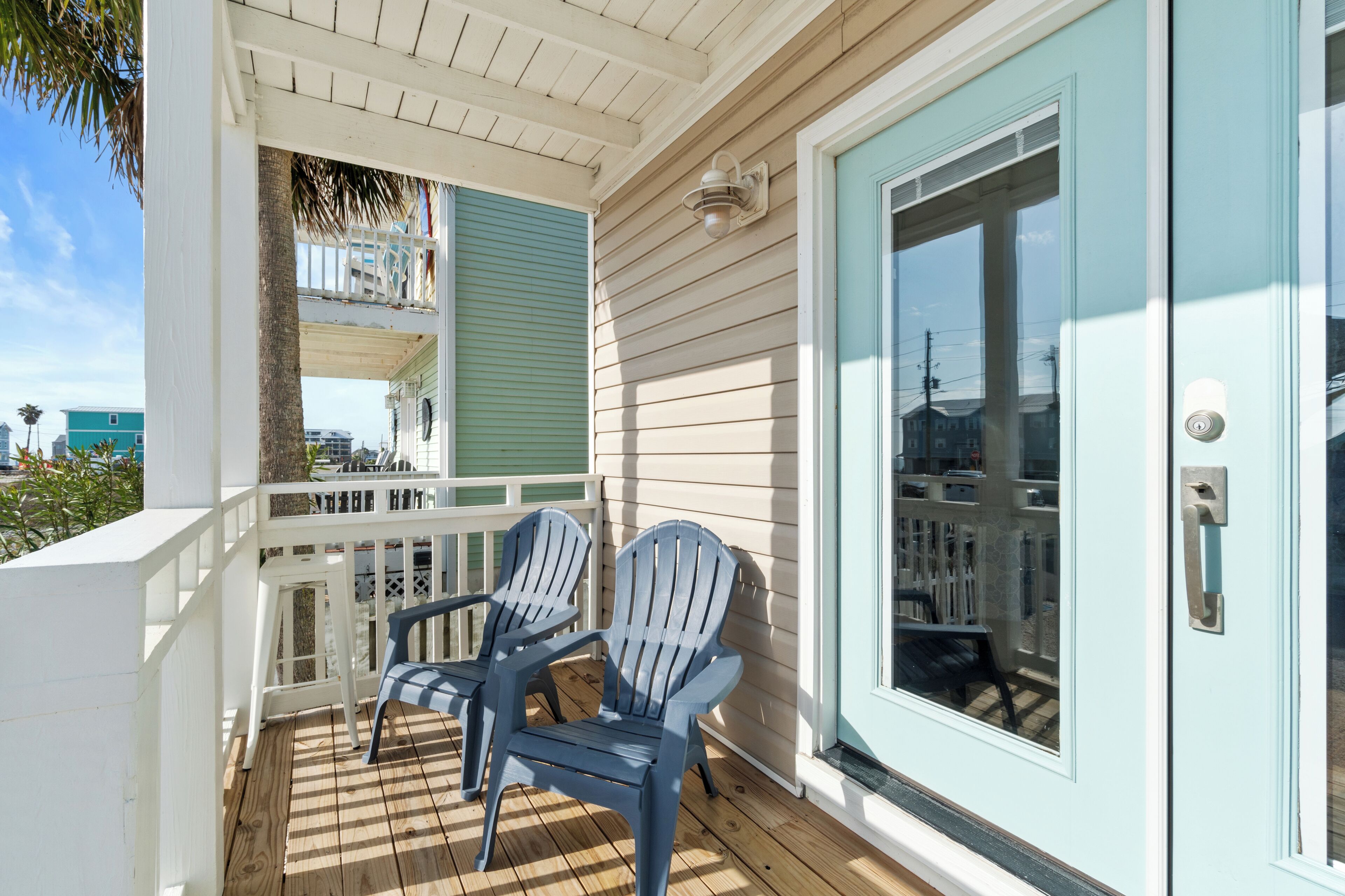 Une terrasse en bois avec deux chaises Adirondack, une rambarde blanche et une porte bleu clair.