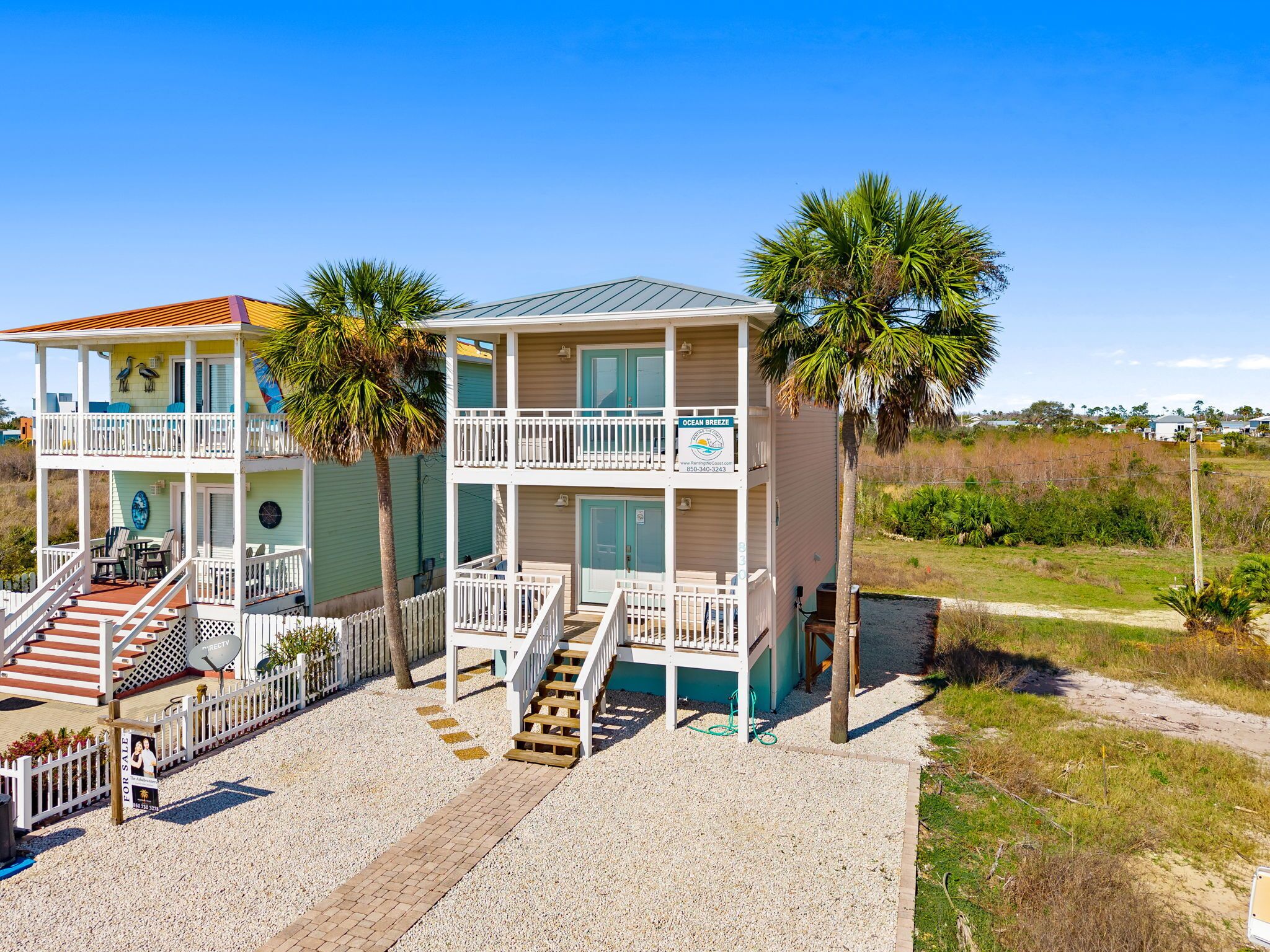 A two-story beachfront property with a balcony, a covered outdoor area, and a gravel driveway.