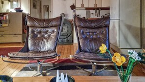 Twee leren fauteuils met metalen frames, een houten tafel en een keuken in de achtergrond.