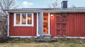 Een rode houten woning met een witte deur en ramen, een schoorsteen en een kleine tuin.