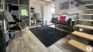 A modern living room with a black rug, wooden furniture, a staircase, and a large window. - La Mine - SAINT MARTIN DU FRESNE (SAINT MARTIN DU FRESNE)