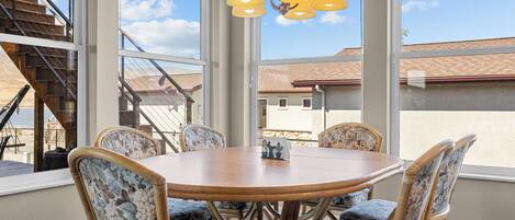 A dining area with a round table and floral-patterned chairs, large windows with a view of a building and a staircase, and a hanging light fixture.