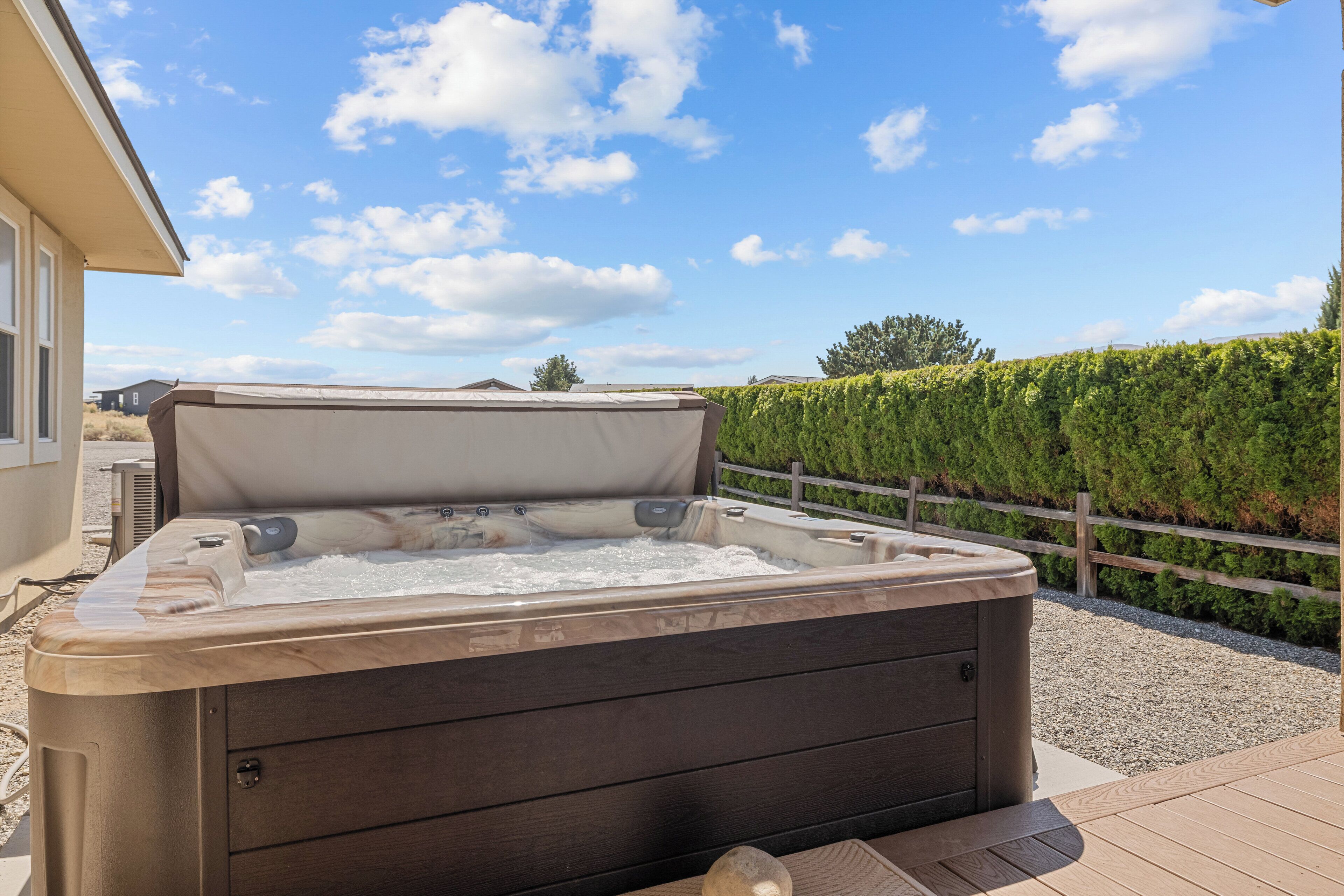 Un bain à remous avec une structure extérieure en bois, installé sur une terrasse en bois devant laquelle se trouve une zone recouverte de gravier.