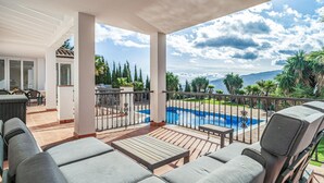 A covered outdoor area with a pool, seating, and a view of the mountains.