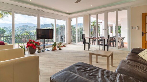 A spacious living area with a flat-screen TV, comfortable seating, and a balcony with a view of the mountains.