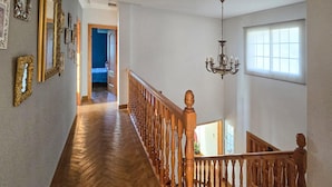 A wooden staircase with a railing, a chandelier, and a hallway with framed pictures on the wall.