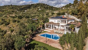 A large house with a swimming pool, surrounded by lush greenery and hills.