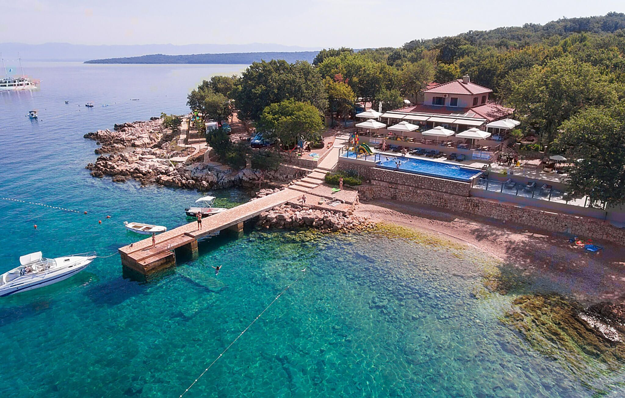 A coastal property with a swimming pool, a dock, and a stone wall.
