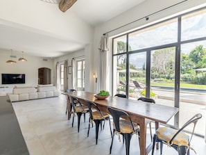 Relax in this serene living room with a long dining table, floor-to-ceiling windows, and a flat-screen TV.