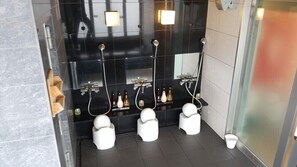 A modern bathroom with black tiled walls, three white toilets, a glass shower enclosure, and a white sink with a mirror. - Myhotel Okazaki (Okazaki)