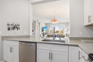 A modern kitchen with white cabinets, a stainless steel dishwasher, and a hanging knife rack.
