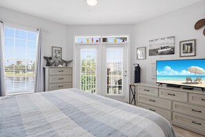 Un dormitorio con cama, televisión, cómoda y balcón con vista al mar.
