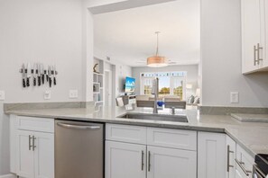 A modern kitchen with white cabinetry, a built-in dishwasher, and a large island with a sink.