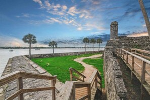 A coastal walkway with a stone wall, wooden railings, and a grassy area.