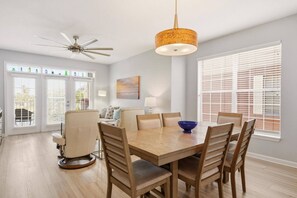 A dining area with a wooden table, chairs, and a blue bowl. There is a ceiling fan and a hanging light fixture. - Atlantis 205C (St. Augustine Beach)