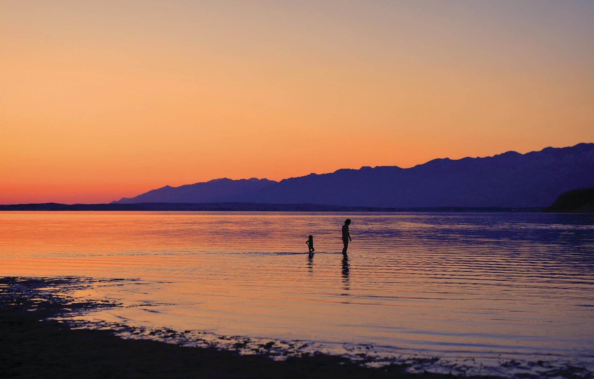 A sunset over a calm body of water with mountains in the background.
