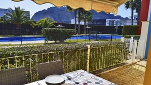 Un coin repas avec une table dressée pour quatre personnes, donnant sur une piscine et des montagnes.