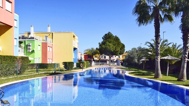 Une piscine à l’eau d’un bleu cristallin, entourée de bâtiments aux couleurs vives et de palmiers.
