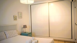 Une chambre d’hôtel avec un lit, une table de chevet avec une lampe, une grande porte coulissante et deux tableaux encadrés au mur.